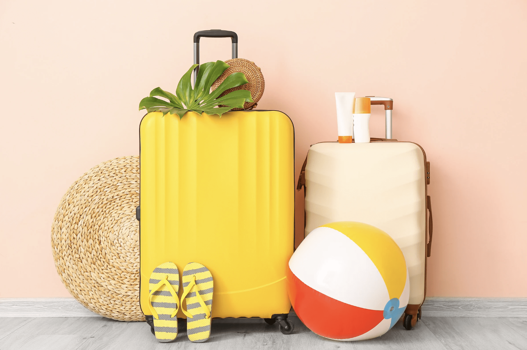 Bright yellow and cream suitcases with summer travel essentials including flip-flops, sunscreen, a beach ball, and a woven hat, perfect for a mindful, recovery-focused vacation.